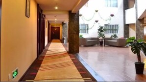 A hotel corridor with a carpeted walkway, a reception desk, and a seating area with plants.
