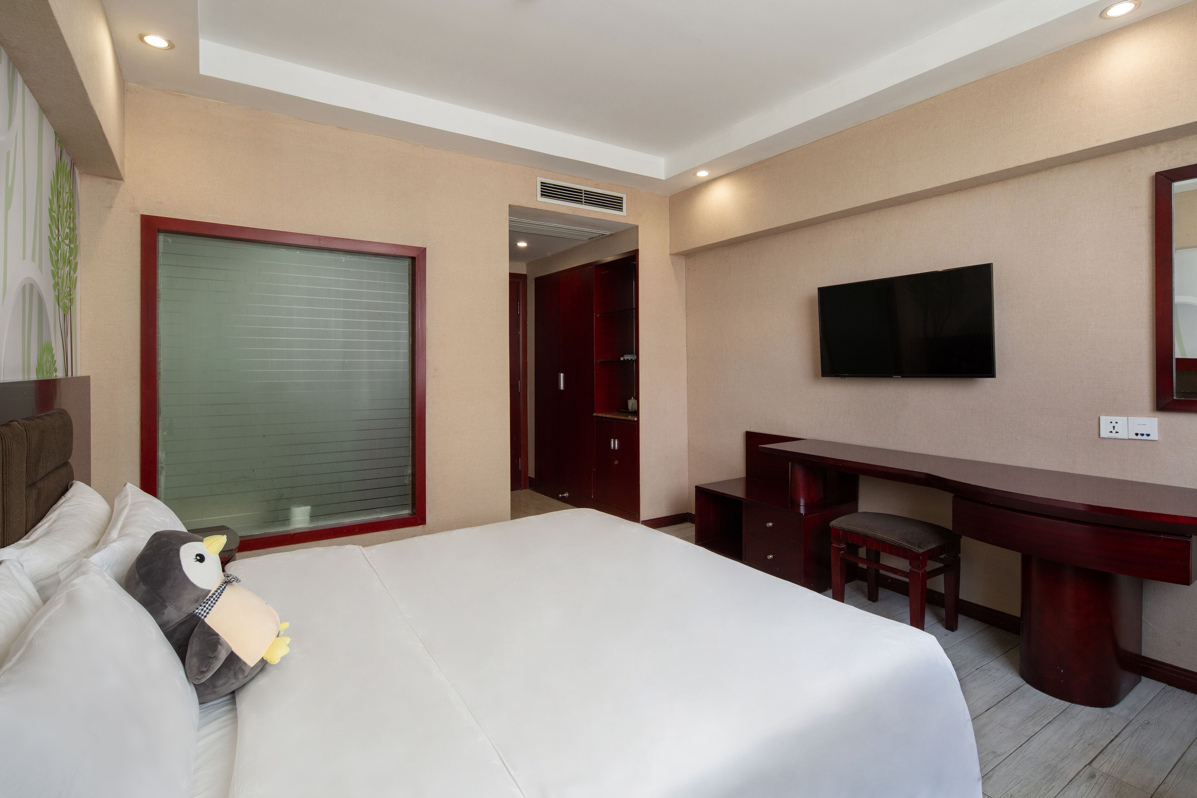 A hotel room with a bed, a desk, a chair, a television, and a wardrobe.
