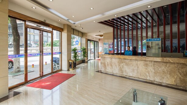 A hotel lobby with a reception desk, large windows, and a red carpet.