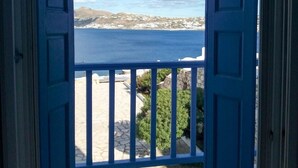 En åben blå dør, der fører ud til en balkon med udsigt over et roligt hav og fjerne bjerge.