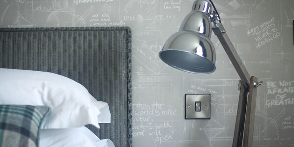 A neatly made bed with a white pillow and a plaid blanket, a modern desk lamp, and a wall with motivational and inspirational writings.