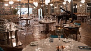 Ein Restaurant mit runden Tischen, transparenten Stühlen und einem Flügel.