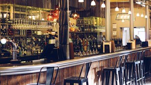Eine Bar mit Holztresen, mehreren hängenden Pendelleuchten und einer Auswahl an Flaschen und Gläsern in Regalen.