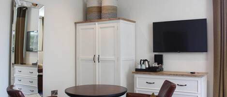 A hotel room with a large mirror, a wardrobe, a television, a round table, and two leather chairs.