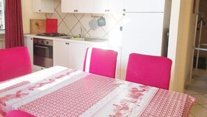 Una cocina compacta con armarios blancos, estufa y pileta. Se observa una mesa de comedor con mantel estampado y sillas rosadas.