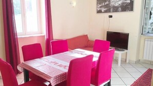 Un comedor con mesa y sillas, televisor y ventana con cortinas.