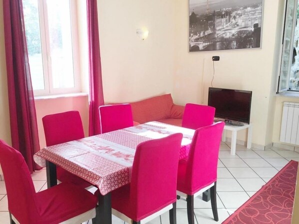 A dining area with a table and chairs, a television, and a window with curtains.