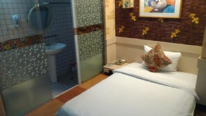 A hotel room with a bed, a bedside phone, a bathroom with a toilet and sink, and a shower area.