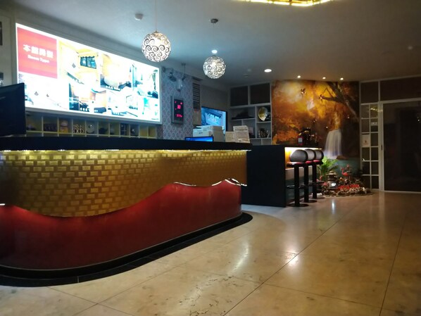 A hotel reception area with a curved counter, a digital screen displaying information, and a wall with a mural.