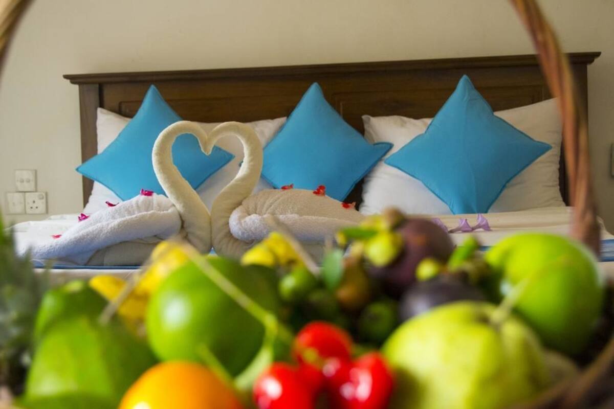 A bed with a heart-shaped towel arrangement and blue pillows.