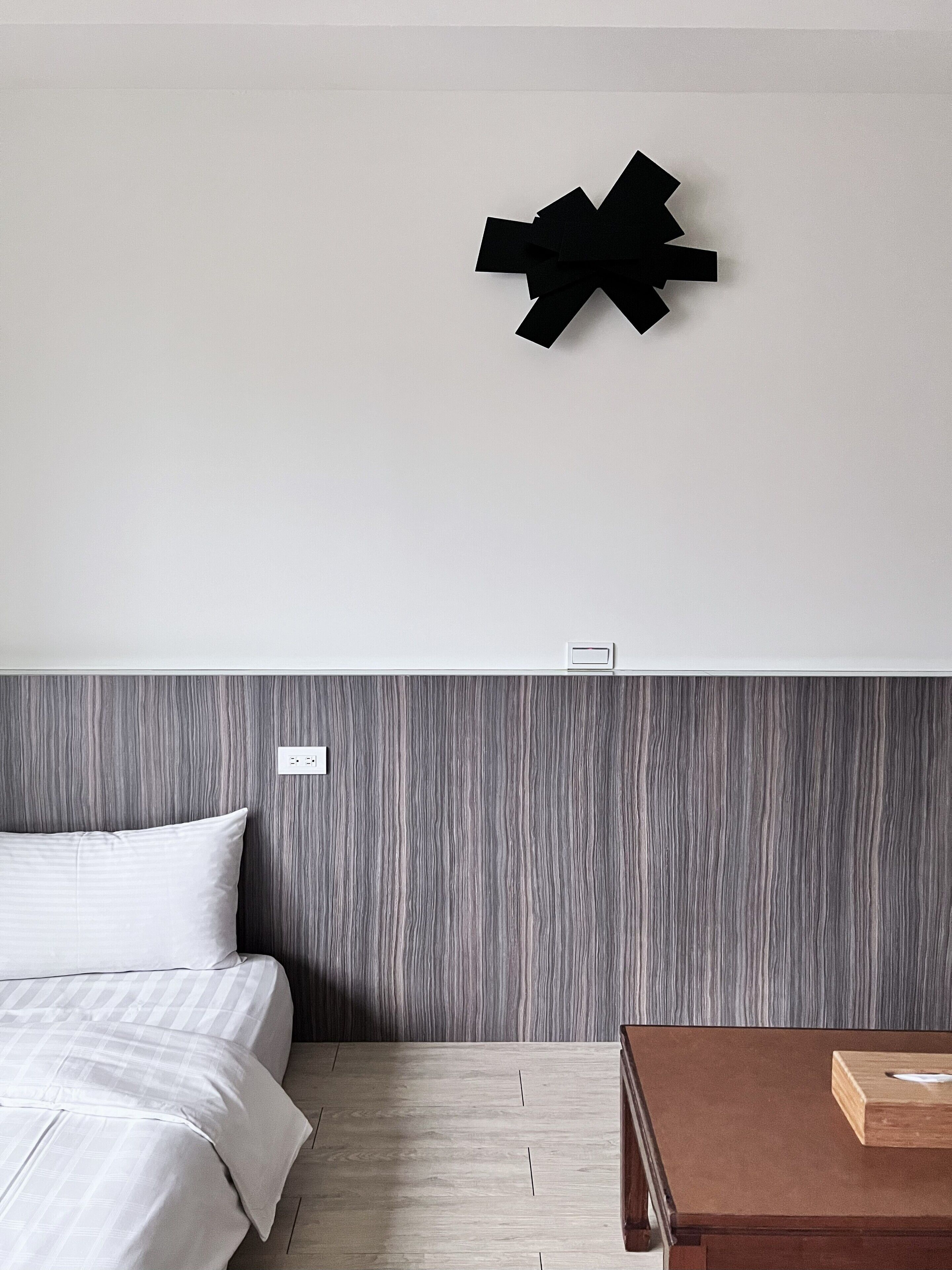 A hotel room with a bed, a wooden nightstand, and a wall-mounted black decorative piece.