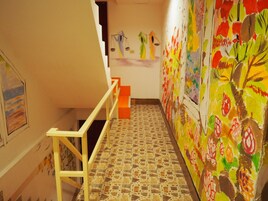 Una escalera con suelo de baldosas y barandilla, que conduce a una habitación con coloridas obras de arte en las paredes.
