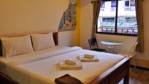 Ein Hotelzimmer mit einem Bett, zwei Stühlen, einem kleinen Tisch und einem Fenster mit Blick auf Gebäude.