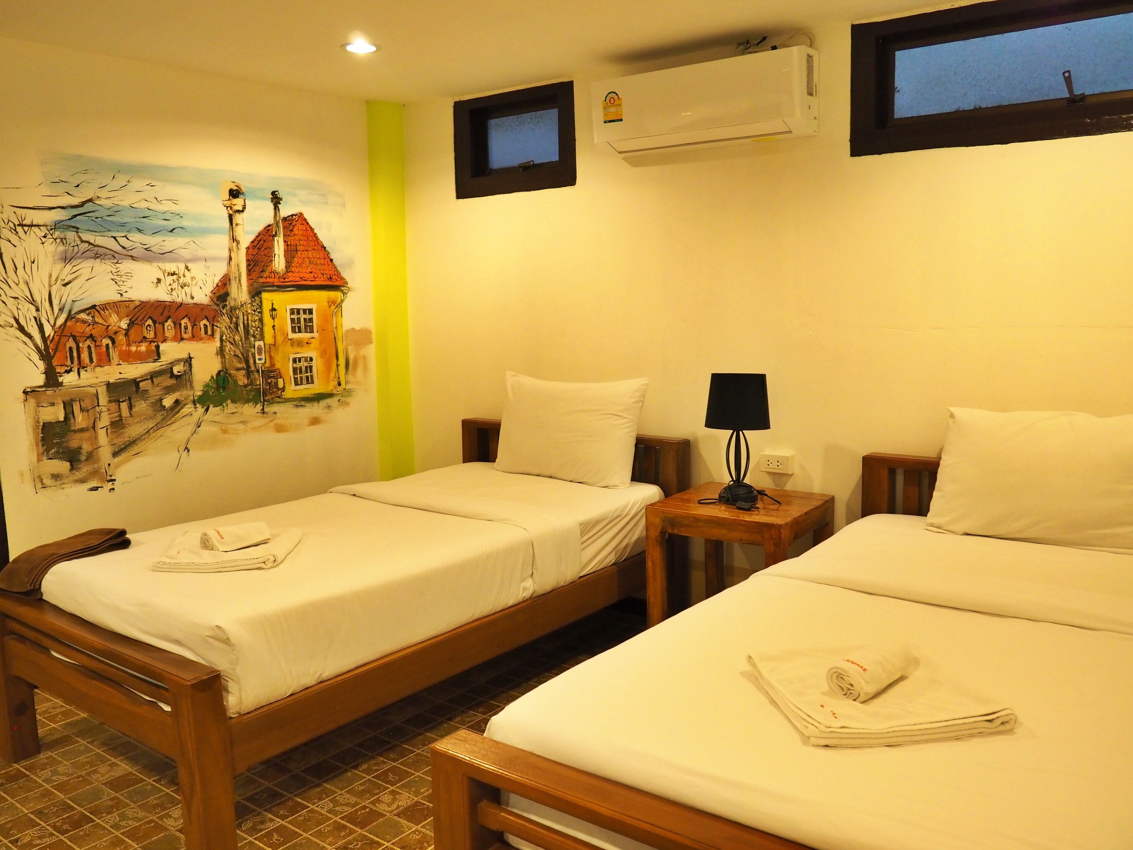 Een hotelkamer met twee eenpersoonsbedden, een klein tafeltje met een lamp, een airconditioning en een wanddecoratie.