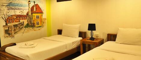 Een hotelkamer met twee eenpersoonsbedden, een klein tafeltje met een lamp, een airconditioning en een wanddecoratie.