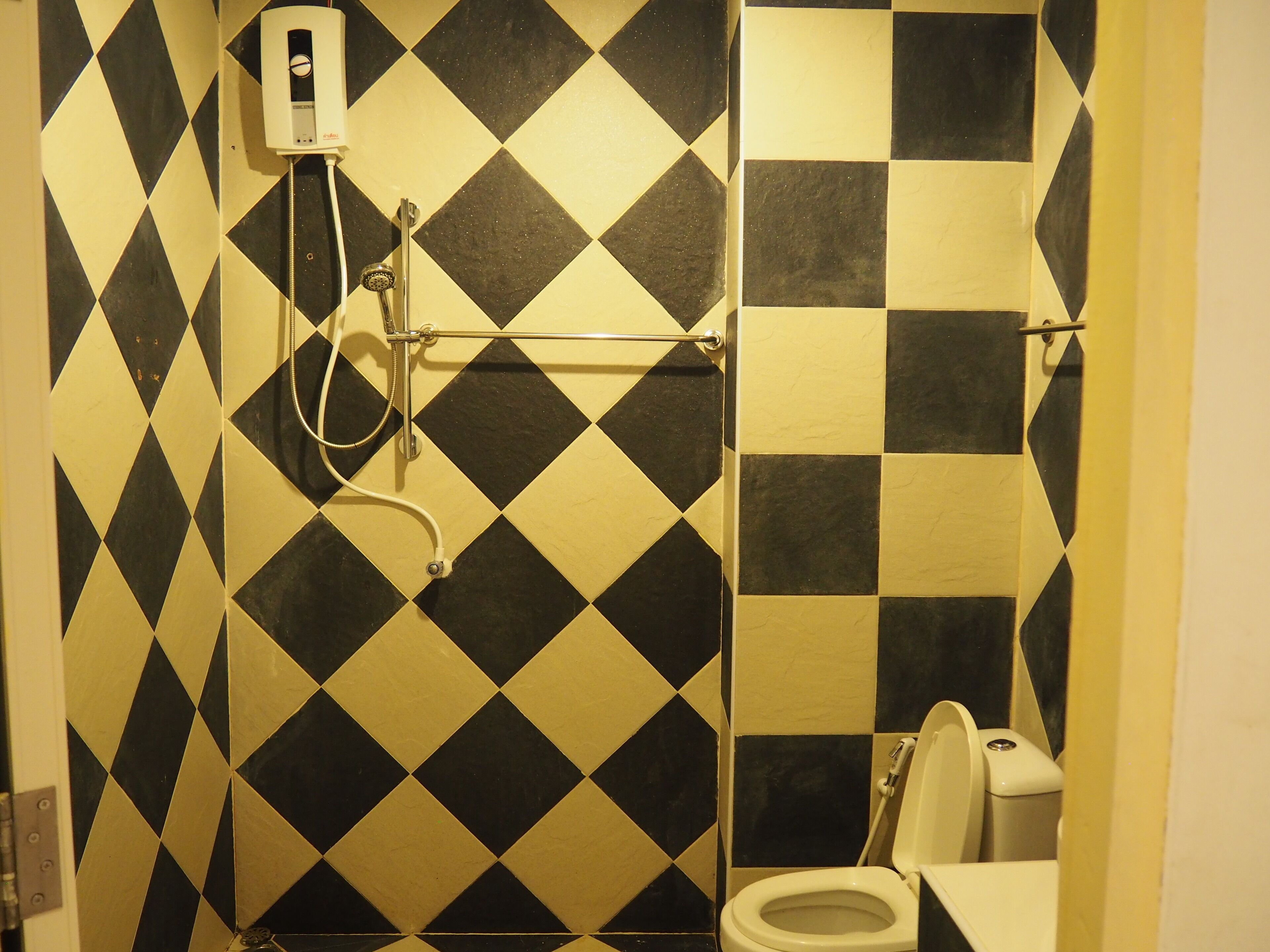 Une salle de bain avec un mur recouvert de carreaux noirs et blancs formant un motif à carreaux, des toilettes et une douche équipée d’un pommeau de douche amovible.