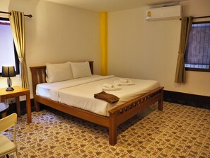 A neatly made bed with white linens and towels, a wooden headboard, a small bedside table with a lamp, and a chair. The room has a tiled floor and a window with curtains. - Baanmaeresidence (Pattaya)