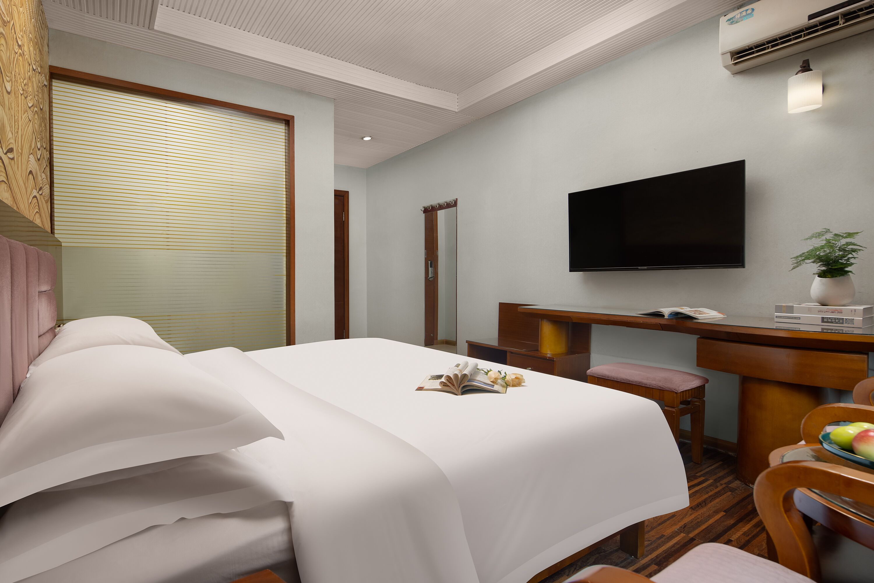 Habitación de hotel con cama, escritorio, silla, televisión y planta en maceta.