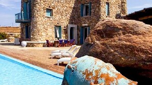 A stone villa with a pool, a large rock, and a cat. - Cavo Nano (Mykonos)