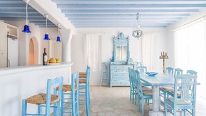 A dining area with a long table and blue chairs, a blue dresser with a mirror, and a chandelier. - Cavo Nano (Mykonos)