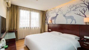 Habitación de hotel con una cama grande, un televisor, un escritorio con lámpara y un mural en la pared con ciervos.