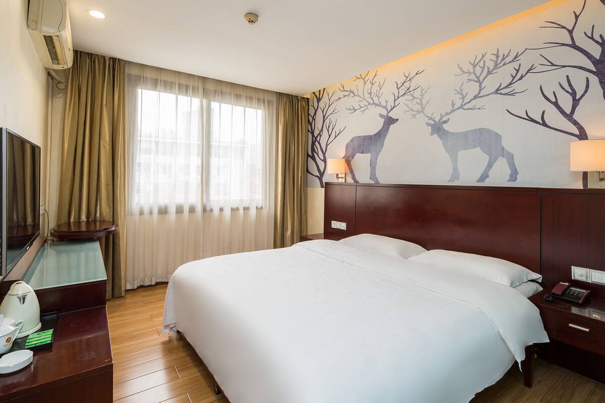A hotel room with a large bed, a TV, a desk with a lamp, and a wall mural of deer.