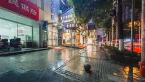 Una calle mojada con un paso de peatones, escaparates y un hidrante rojo.