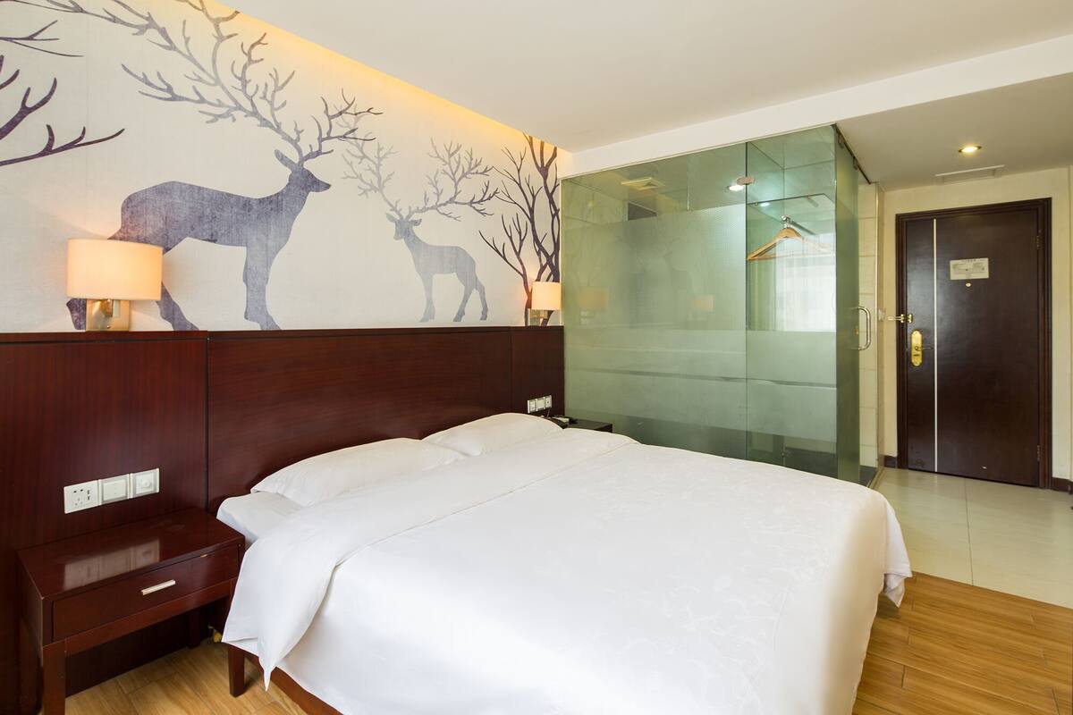 A hotel room with a large bed, a nightstand, a lamp, and a wall mural of deer.