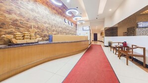Zona de recepción de hotel con un mostrador curvo, alfombra roja y una pared con textura.