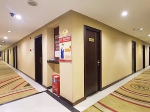 A hotel corridor with doors, a fire extinguisher, and a poster on the wall.