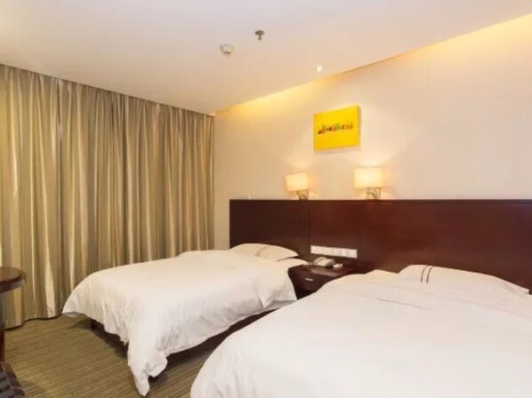 A hotel room with two beds, a large window with curtains, a nightstand with a lamp, and a sign on the wall.