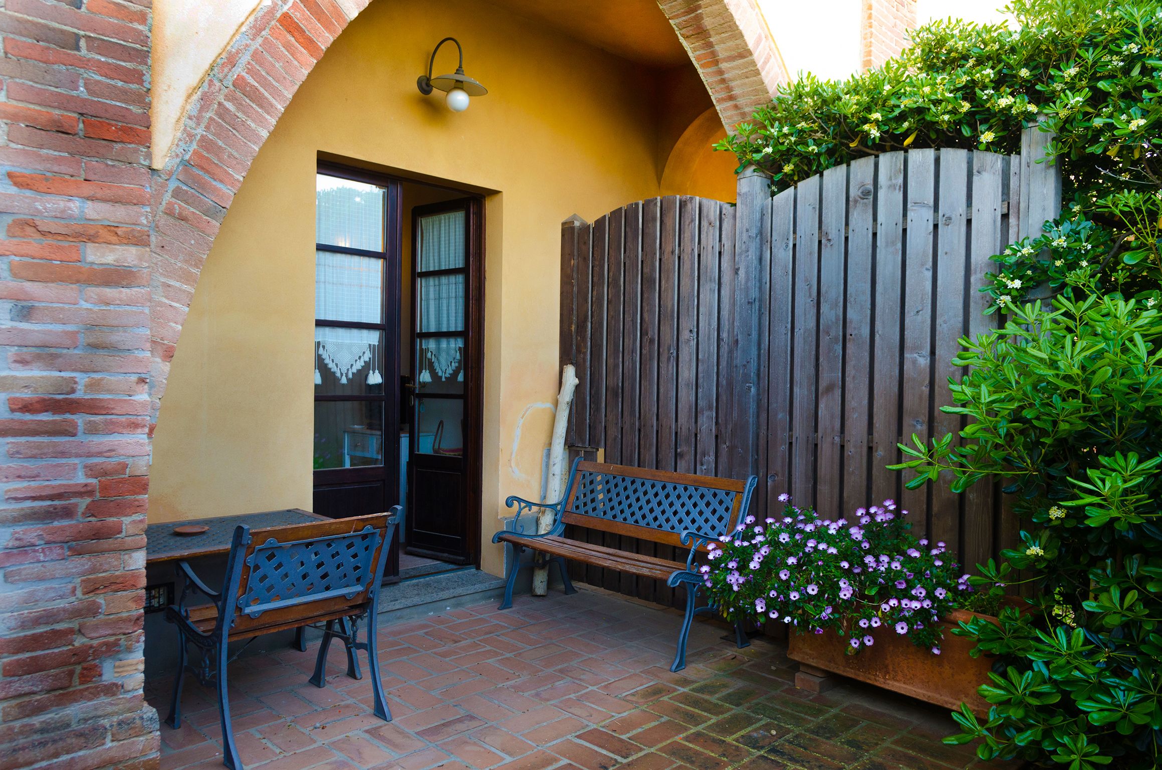 Un patio con un banco de madera, una mesa y una planta en maceta con flores.
