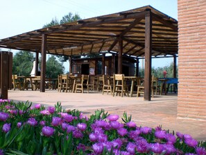 An outdoor seating area with wooden tables and chairs under a wooden pergola.