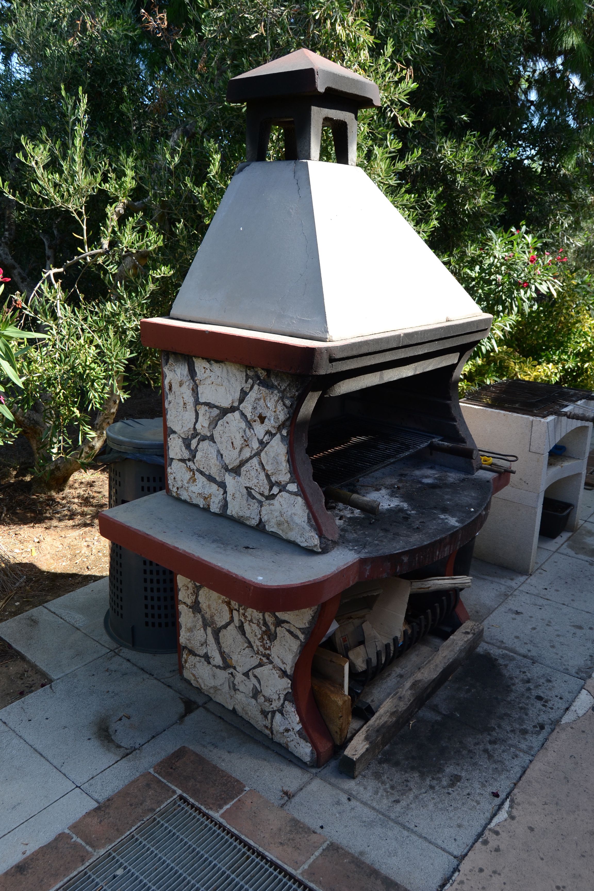 A stone-built outdoor grill with a chimney, surrounded by greenery.