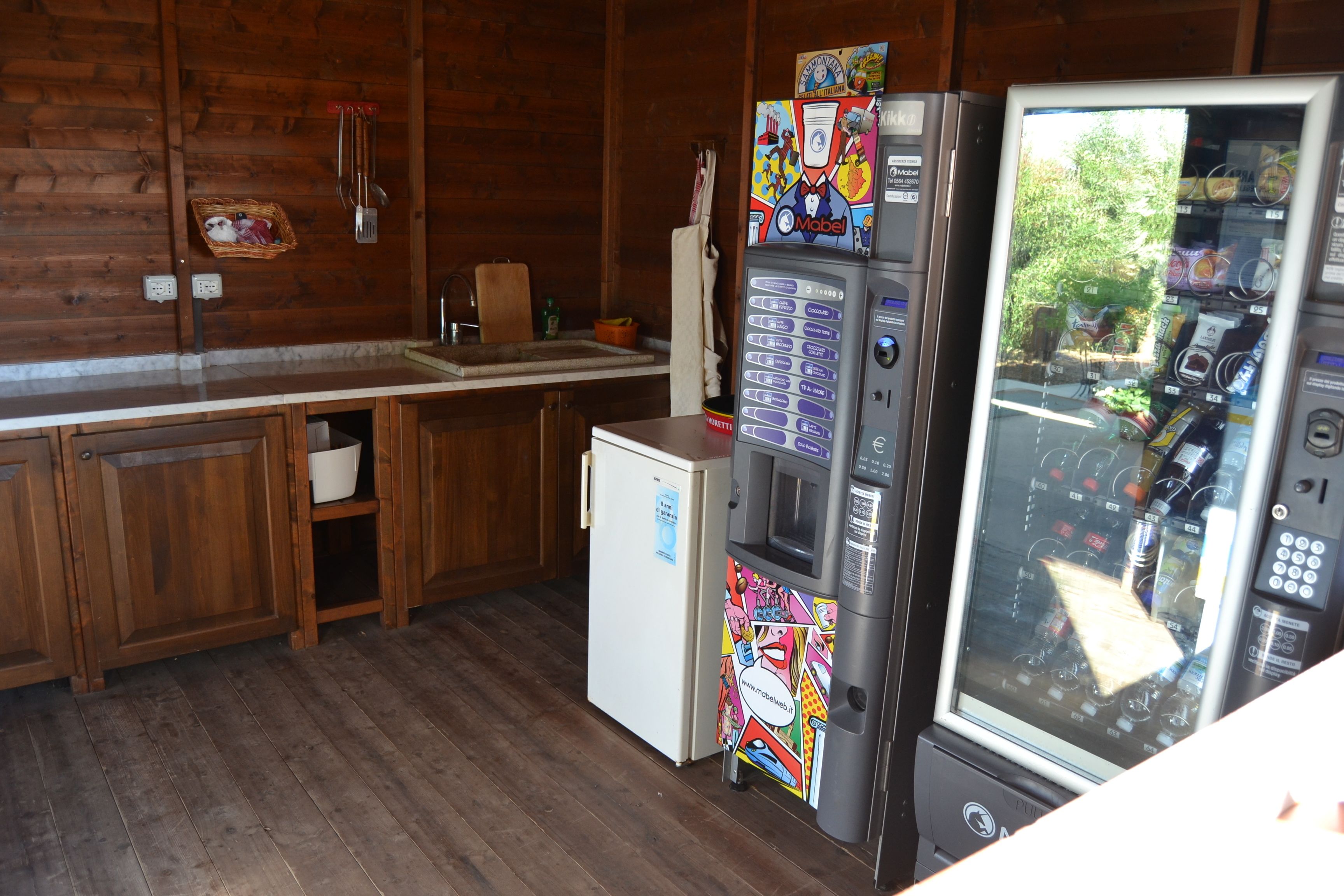 A kitchen with wooden cabinets, a refrigerator, a microwave, and a vending machine.