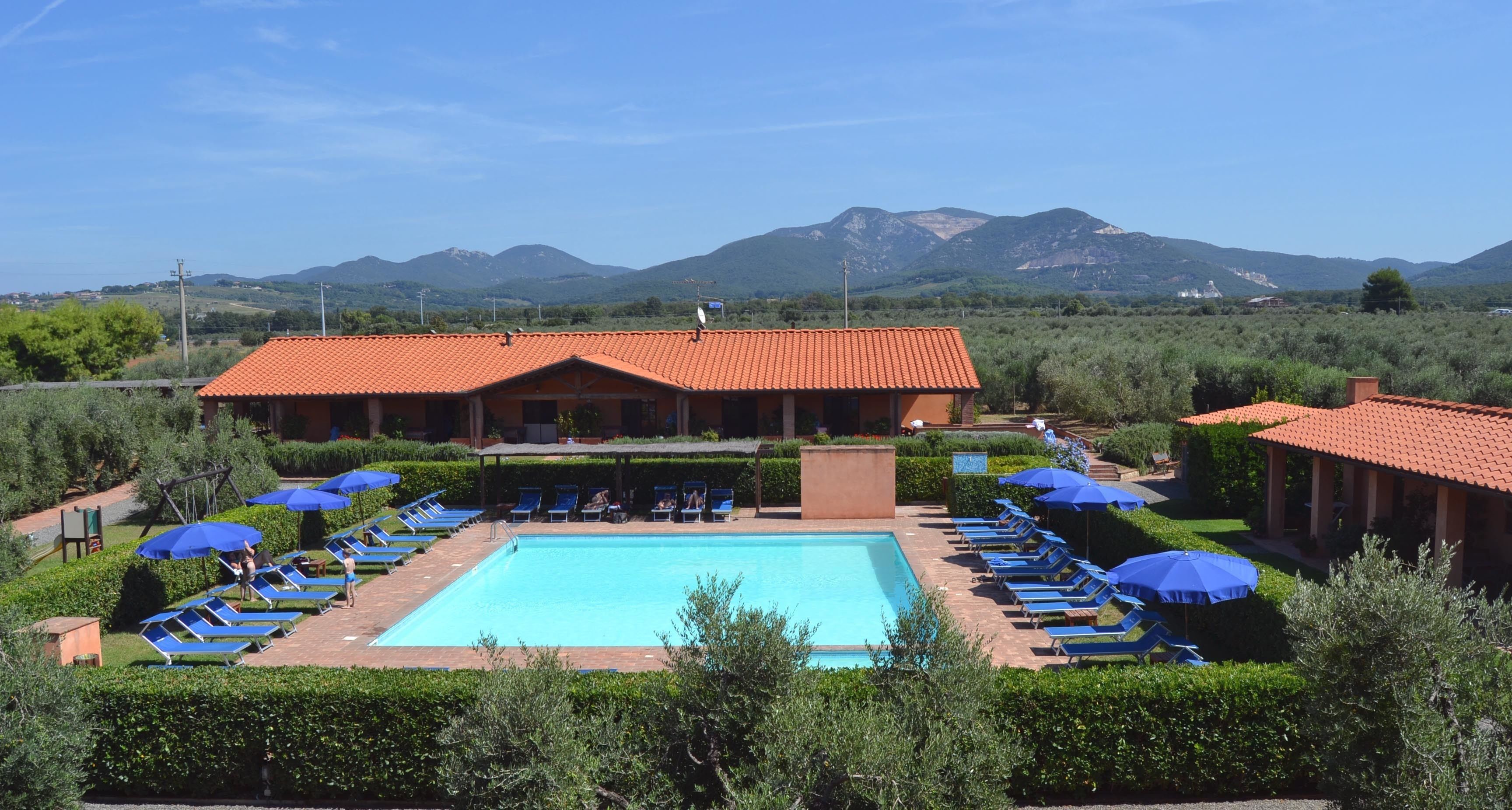 Área de piscina com espreguiçadeiras e guarda-sóis, cercada por vegetação e com vista para montanhas.