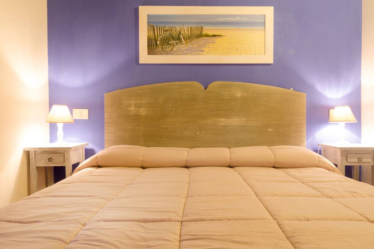 Ein Bett mit Kopfteil, zwei Nachttische mit Lampen und ein gerahmtes Bild an der Wand.