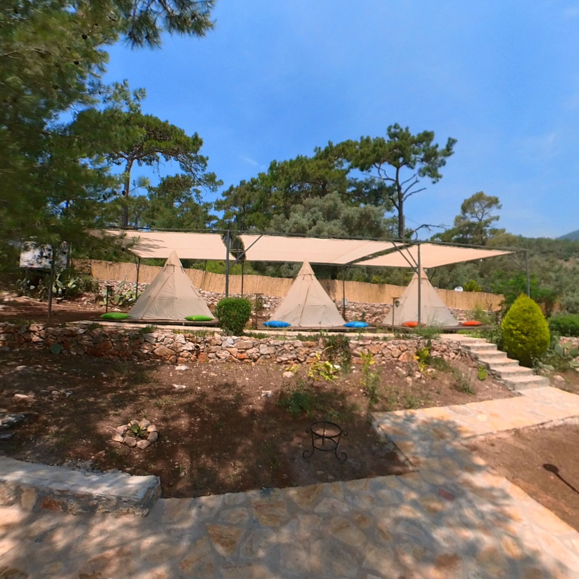 Un camping con varias tiendas de campaña, senderos de piedra y un muro de piedra.