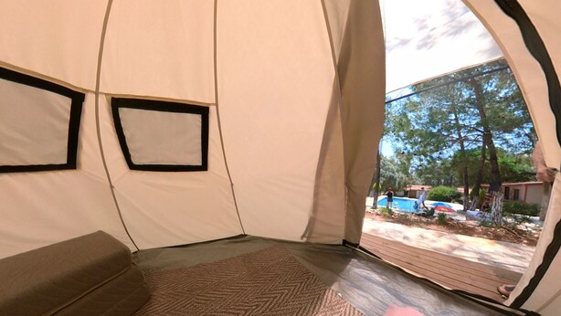 Une tente comprenant un espace de couchage, une fenêtre et donnant sur un quartier résidentiel.