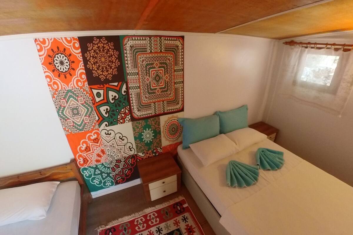 A cozy bedroom with a bed, pillows, a small table, and a wall adorned with colorful patterns.