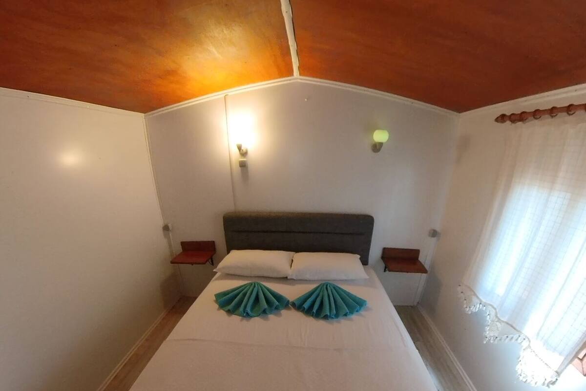 A hotel room with a bed, two bedside tables, and a window with curtains.