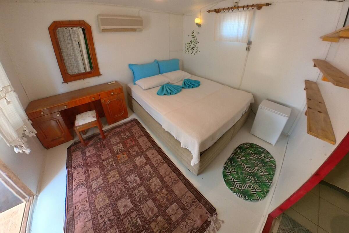 A bedroom with a bed, a desk, an air conditioner, a window, and a wall-mounted light fixture.