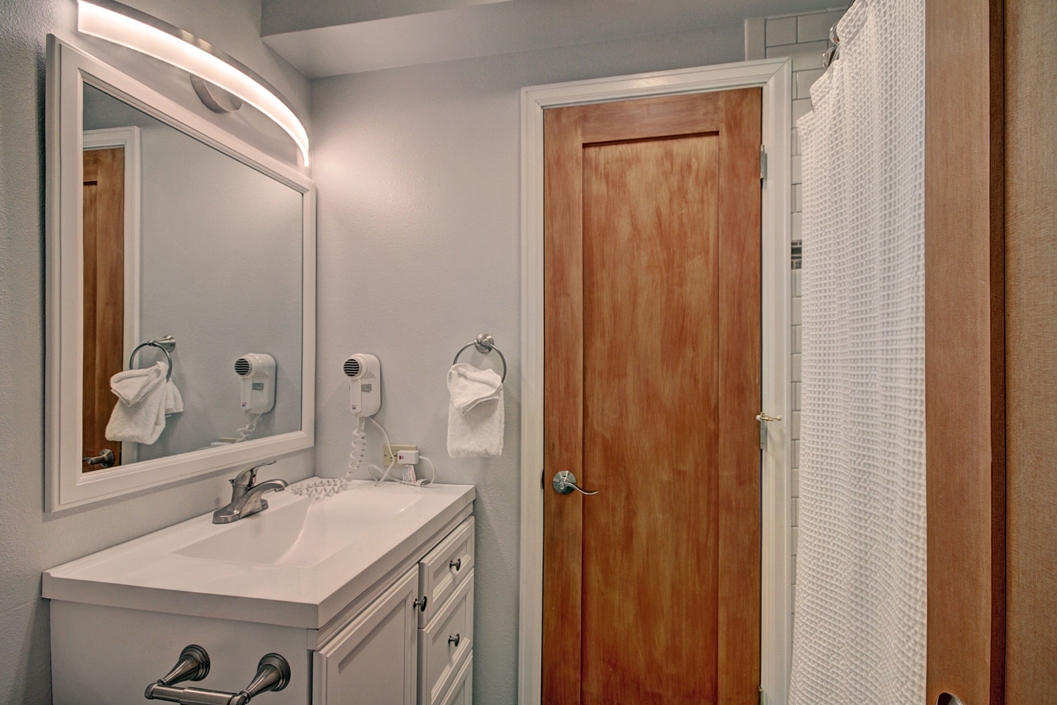 A bathroom with a white sink, a mirror, a towel rack, a wooden door, and a shower curtain.