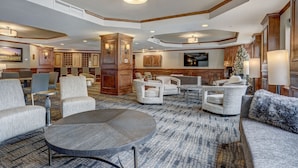 A spacious lobby with a large round table, several sofas, and armchairs. There is a wooden cabinet and a Christmas tree.