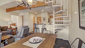 A modern living room with a dining table, comfortable seating, a staircase, and a chandelier.