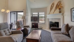 A spacious living room with a fireplace, comfortable seating, and a large window offering a view of the outdoors.