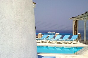 A poolside area with lounge chairs and a view of the sea. - Villa Adonis (Mykonos)