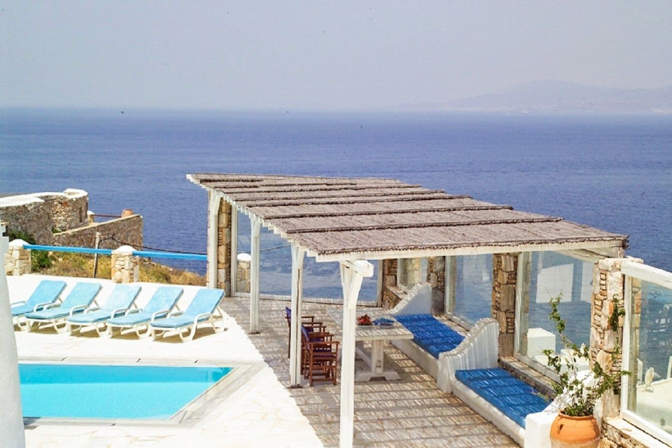 A poolside area with blue lounge chairs, a covered seating area, and a view of the sea.