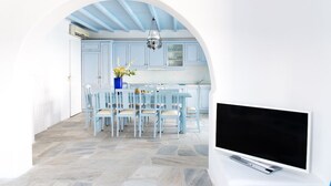 Una cocina moderna con armarios azules, un comedor con sillas azul claro y un televisor de pantalla plana sobre un soporte blanco.