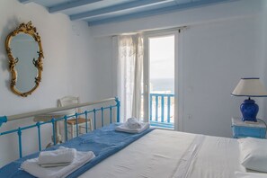 A room with a bed, a blue railing, a white door, and a view of the sea. - Villa Adonis (Mykonos)
